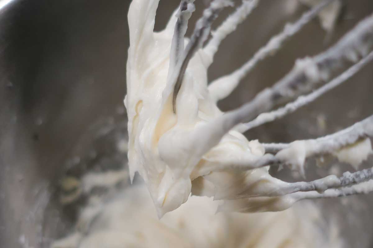 Close-up of cream cheese frosting being whipped in a stand mixer for Crumbl-style gluten-free sugar cookies