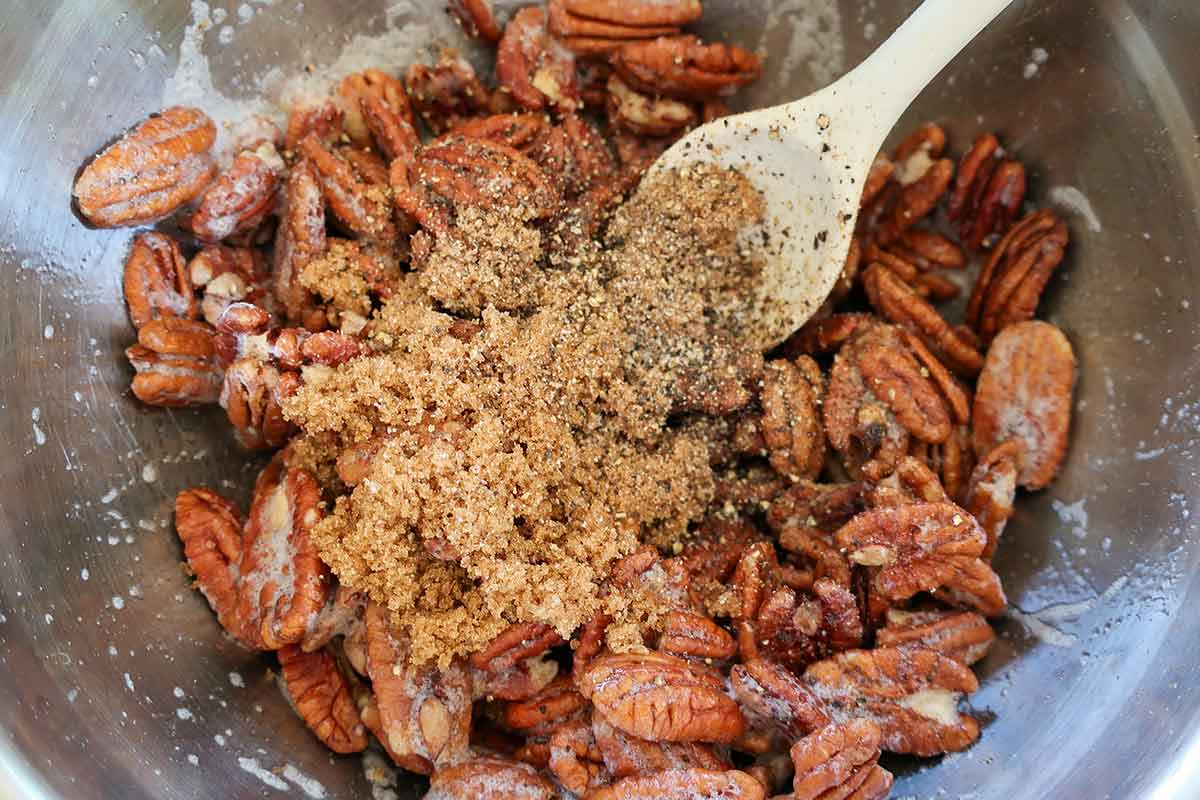 raw pecans in a bowl with egg white mixture, maple syrup, brown sugar & spices