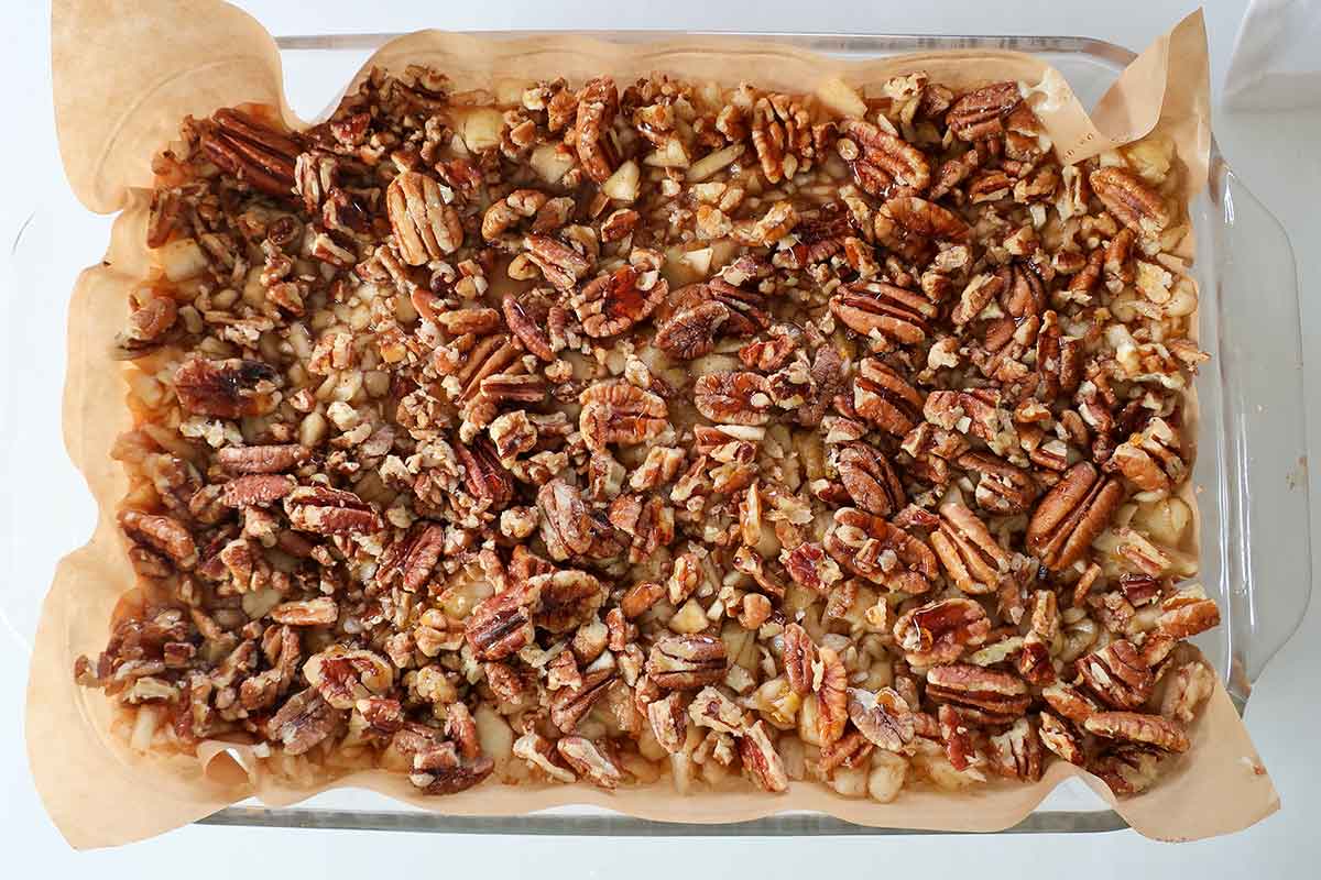 Chopped pecans sprinkled and maple syrup drizzled over apple layer on gluten-free cake before baking