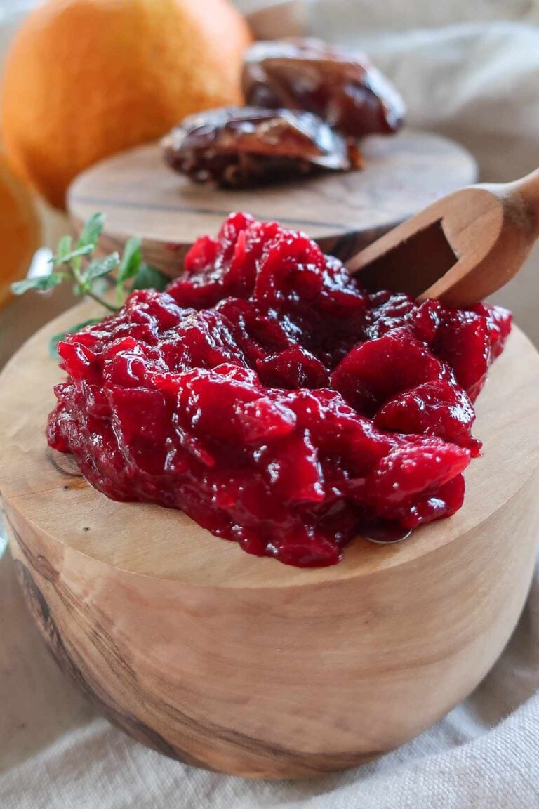 Bright cranberry orange chutney with dates in a bamboo bowl, with whole dates and fresh orange in the background