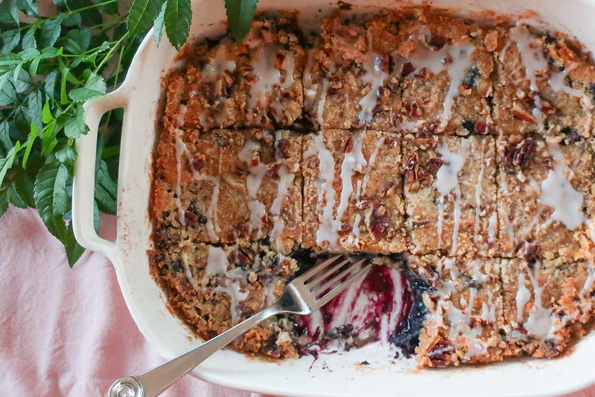baked gluten free berry dump cake with golden topping and bubbly blueberry filling peeking on the side of the baking dish