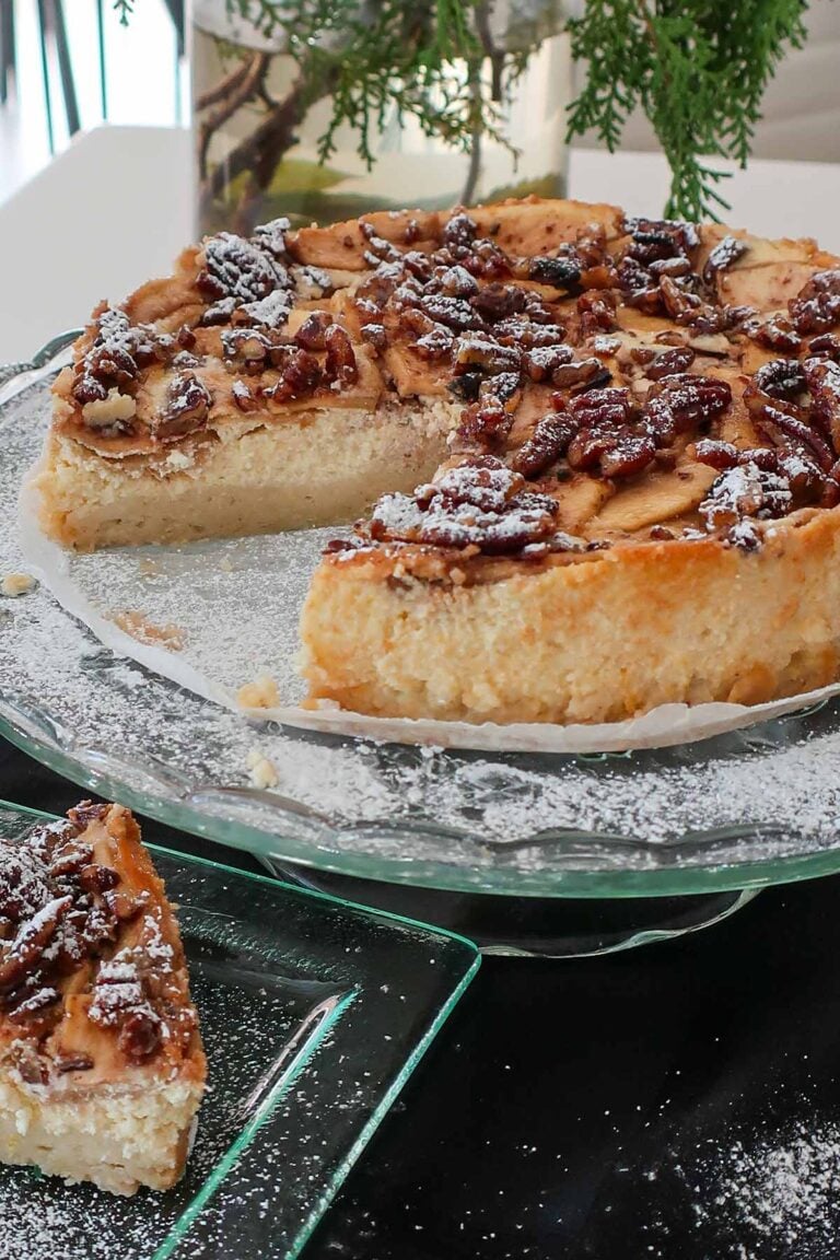 danish ricotta apple cake on a cake platter showing creamy inside and topped with pecans dusted with powdered sugar