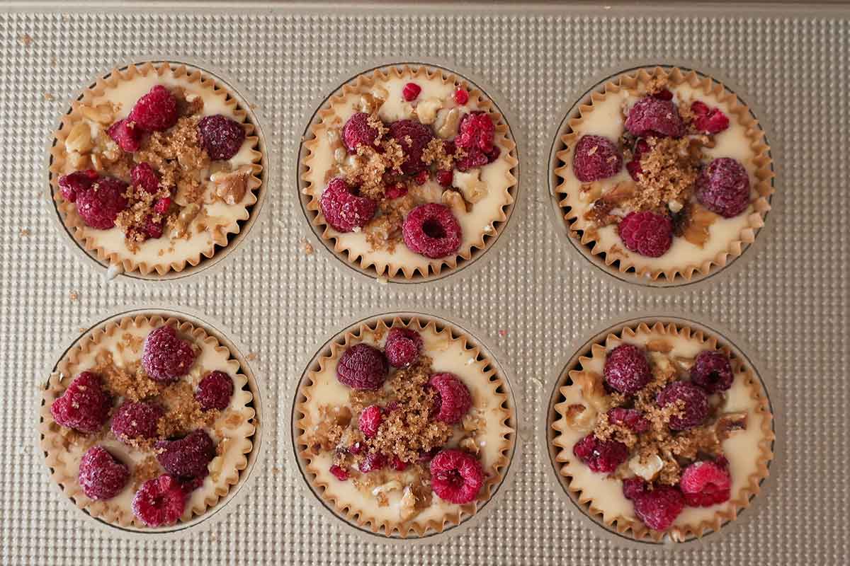 gluten free pancake muffin batter in a muffin pan topped with berries and nuts before baking