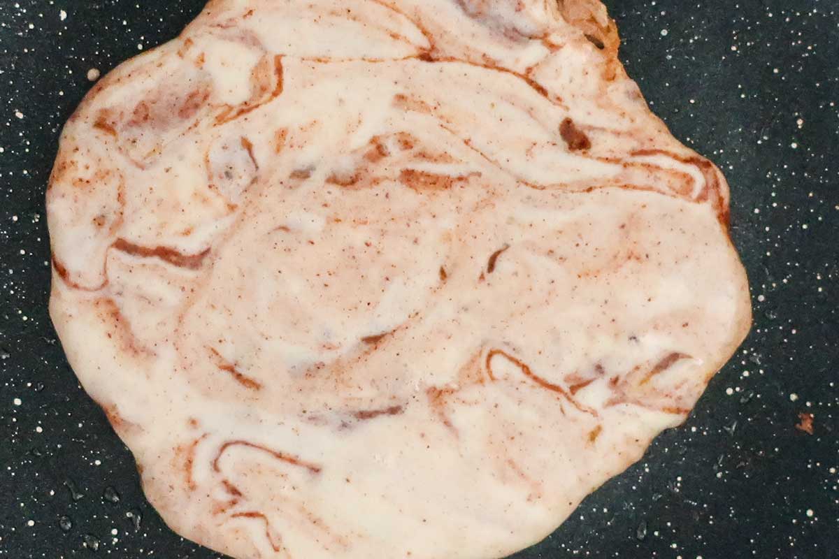 Pancake batter in skillet with cinnamon cream cheese swirled in the batter before flipping. 