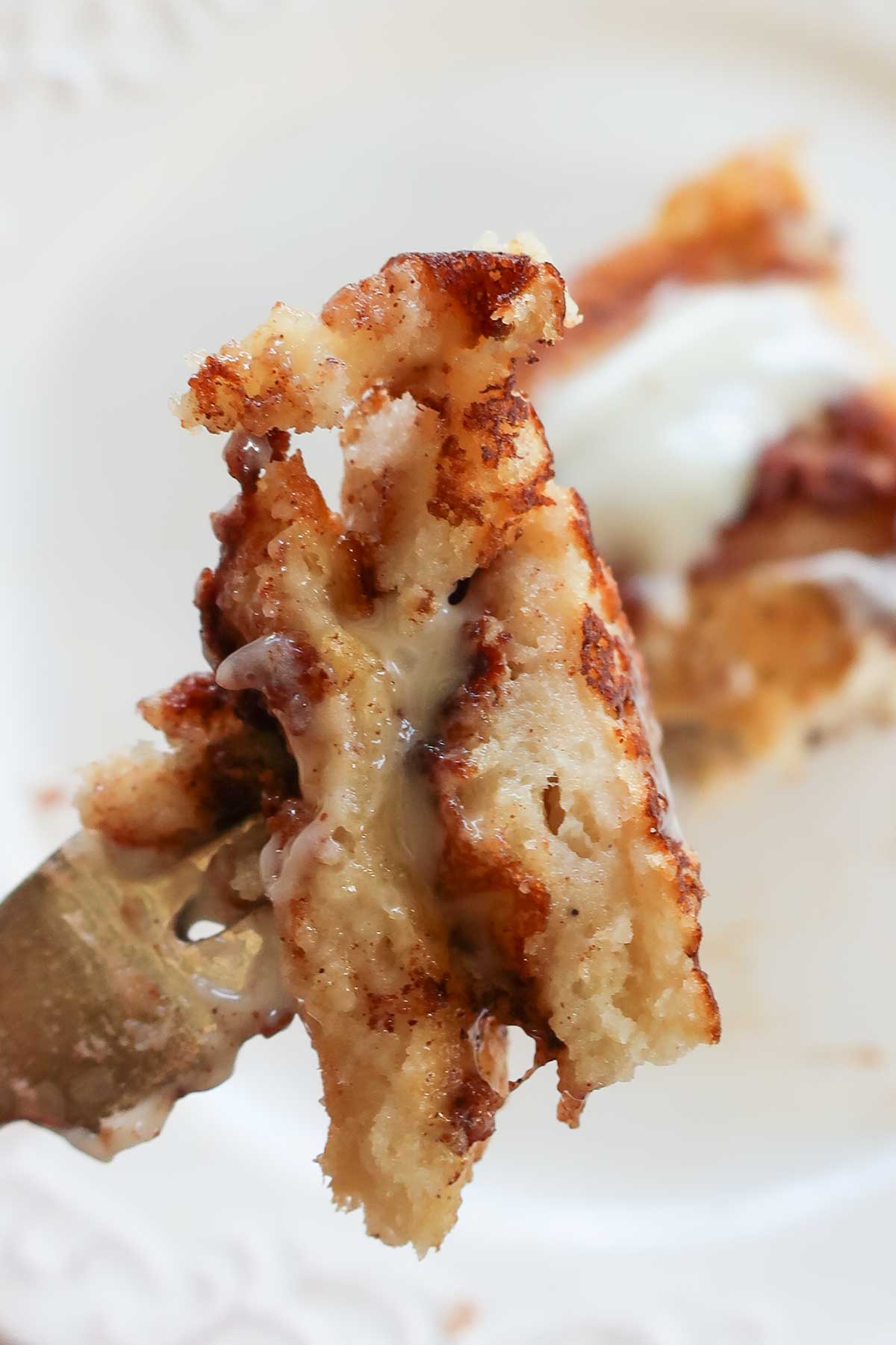 Piece of vegan cinnamon roll pancake on a fork smothered in cream cheese frosting