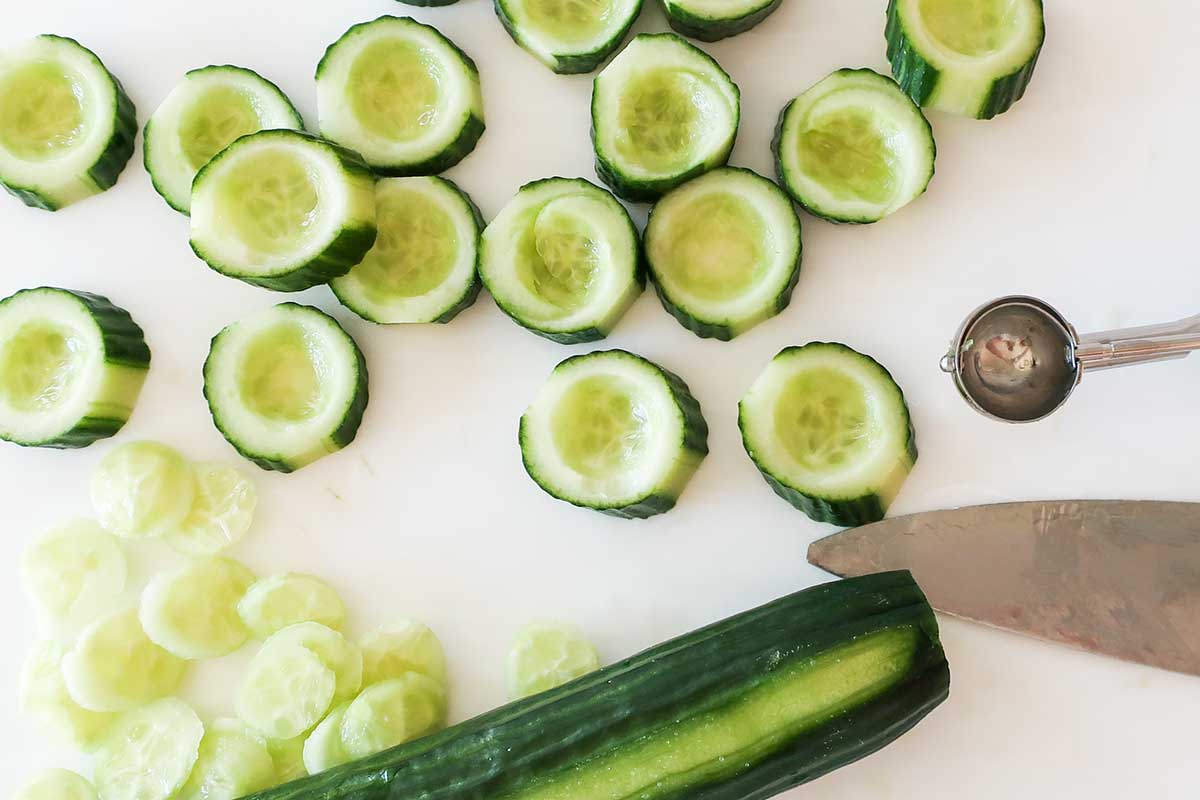 Melon baller scooping out cucumber centers to create cups for filling 