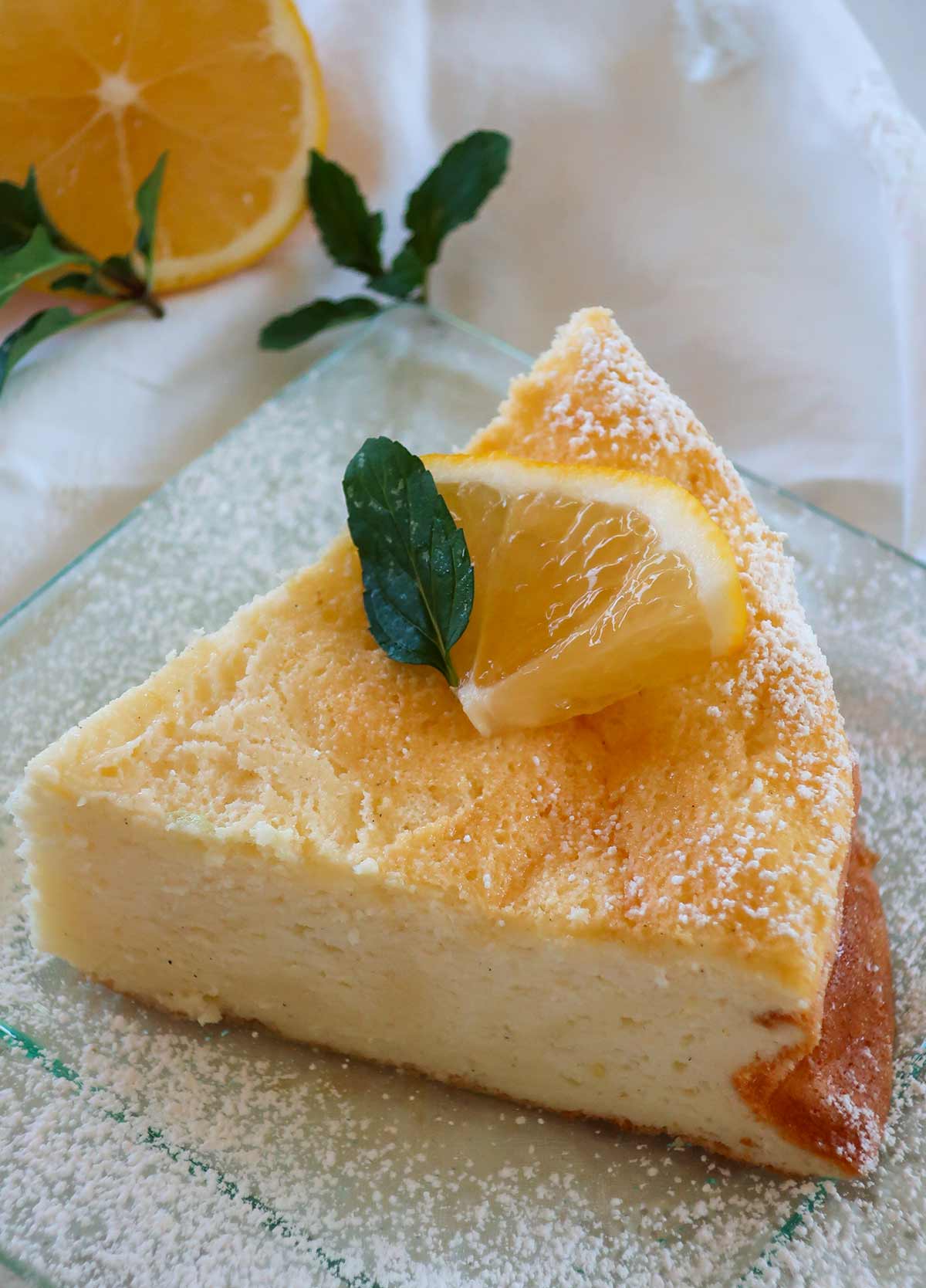 top view of a slice of lemon cloud cake decorated with mint, powdered sugar and a lemon slice on a clear plate