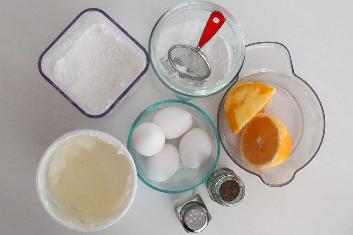 Flat lay of 5-ingredient cake components: fresh eggs, Greek yogurt, whole lemons, and potato starch on a marble counter.