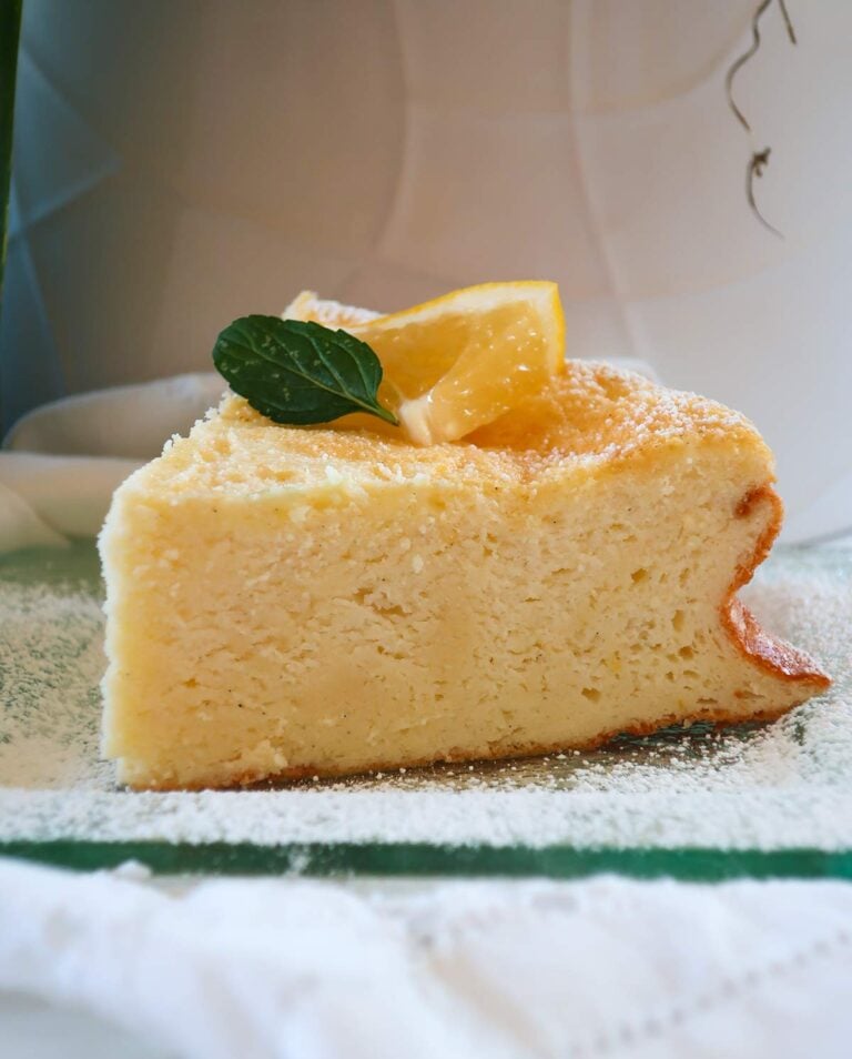 A slice of Lemon Cloud Yogurt Cake on a glass plate, dusted with powdered sugar and topped with lemon slice and mint