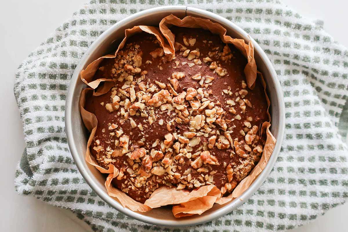 baked grain-free chocolate banana cake batter in a round baking pan topped with walnut pieces