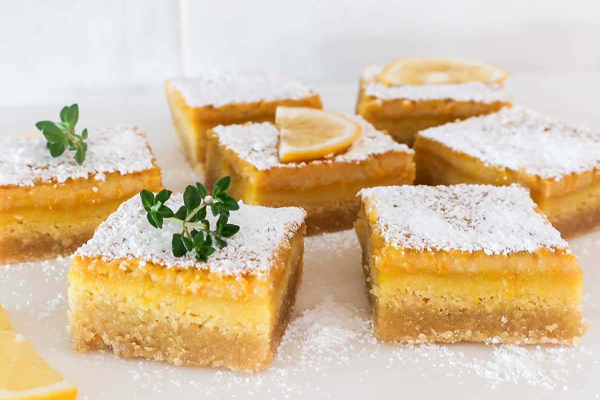 close up of square maple lemon bars GF and DF on a white plated dusted with powdered sugar and green garnish