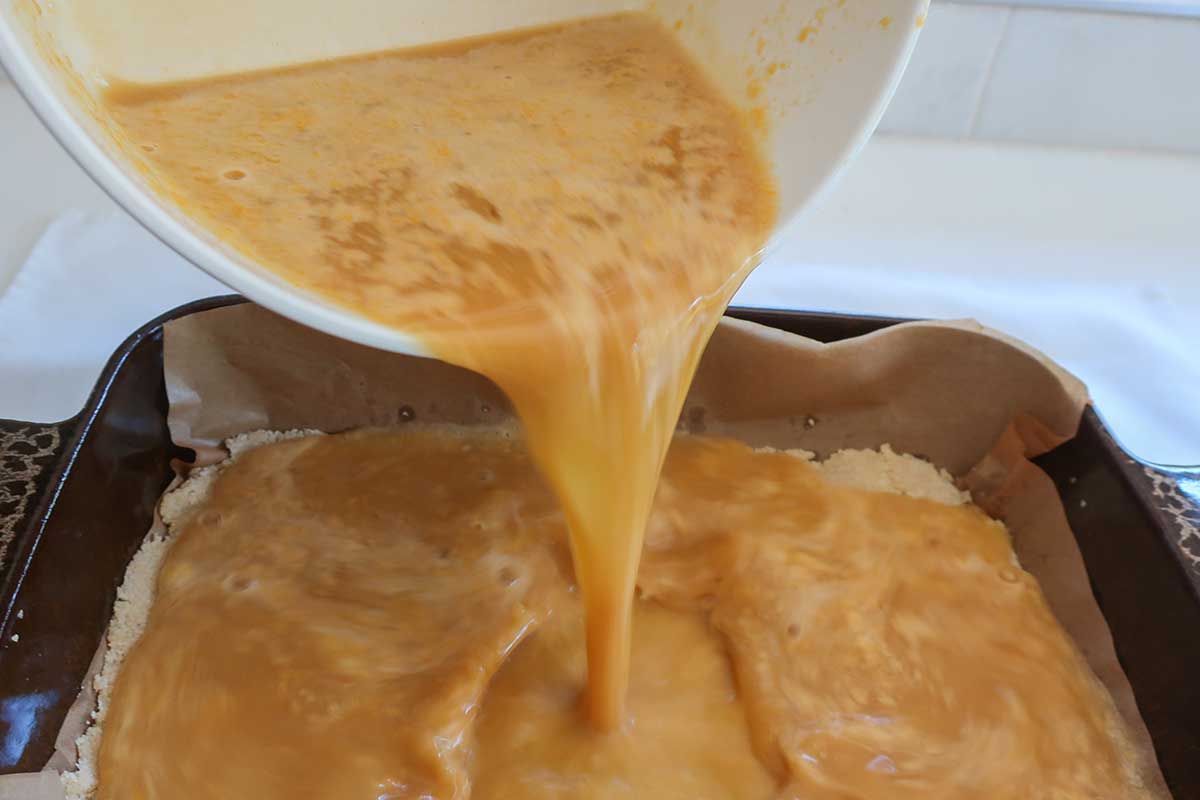 pouring the lemon filling over the freshly baked hot marzipan crust