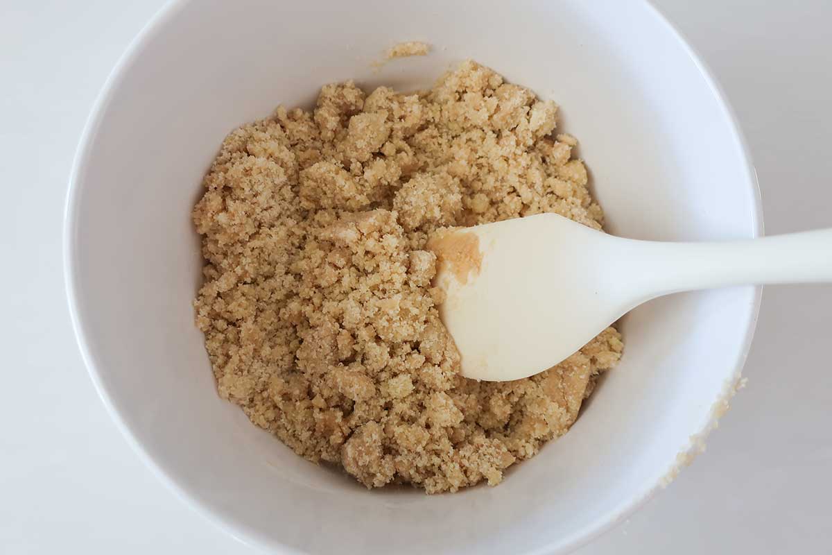 a mixture for the crust, amond flour, rice flour, maple syrup and olive oil in a bowl looks like wet sand