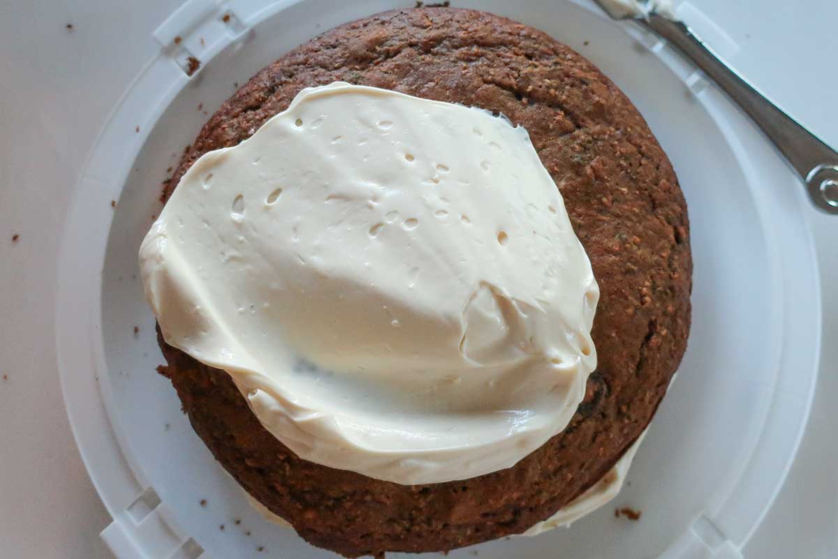 spreading cream cheese frosting over carrot cake layers