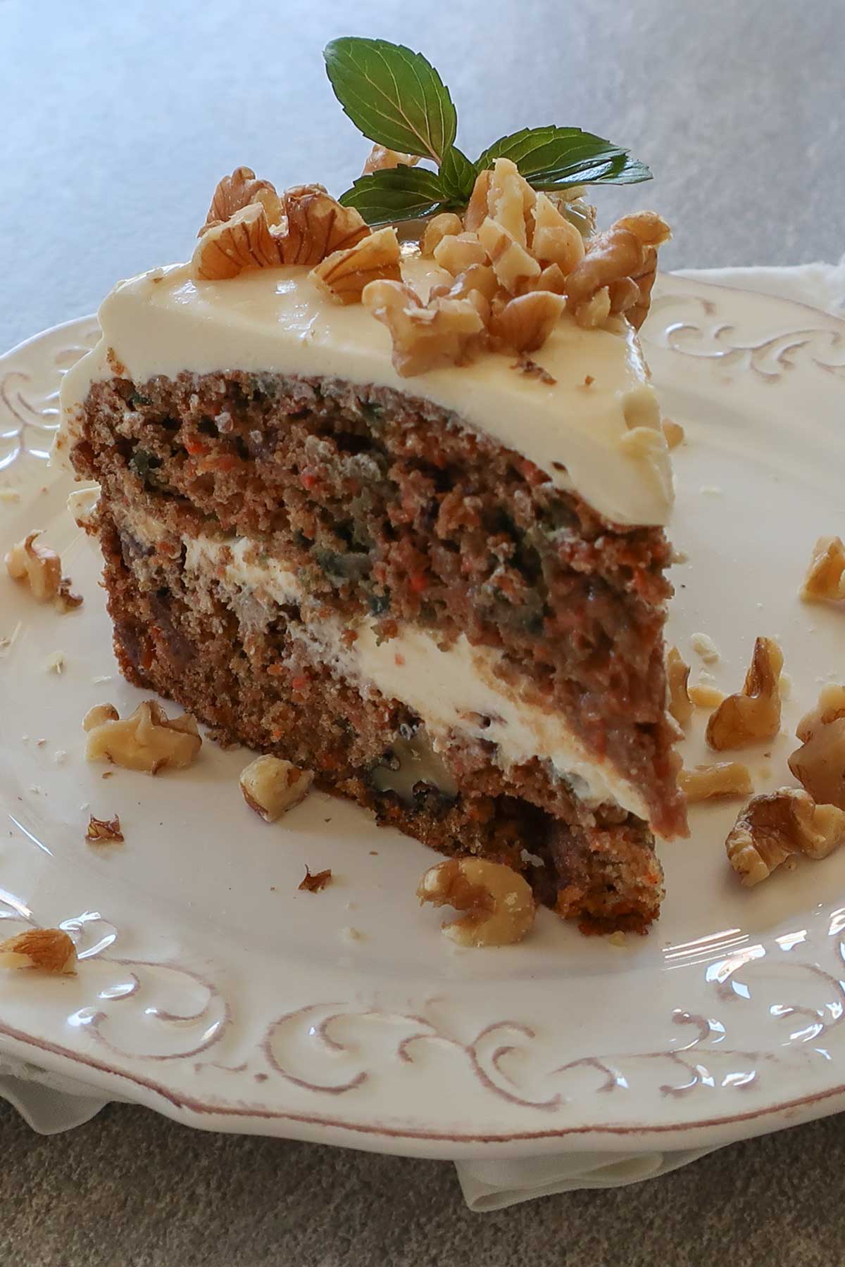 slice of carrot cake with cream cheese frosting and chopped walnuts on a dessert plate 