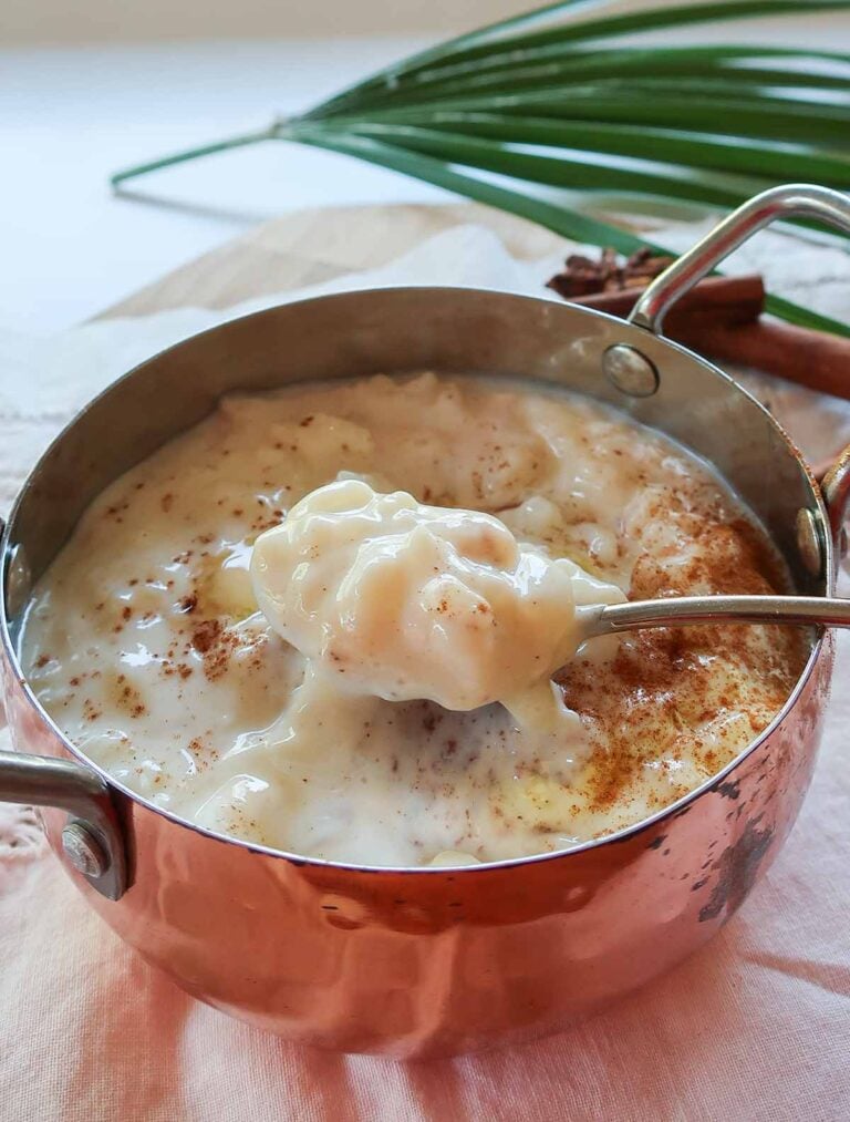 Creamiest gluten-free rice pudding in a rustic copper bowl with a spoon filled with creamy pudding topped with cinnamon
