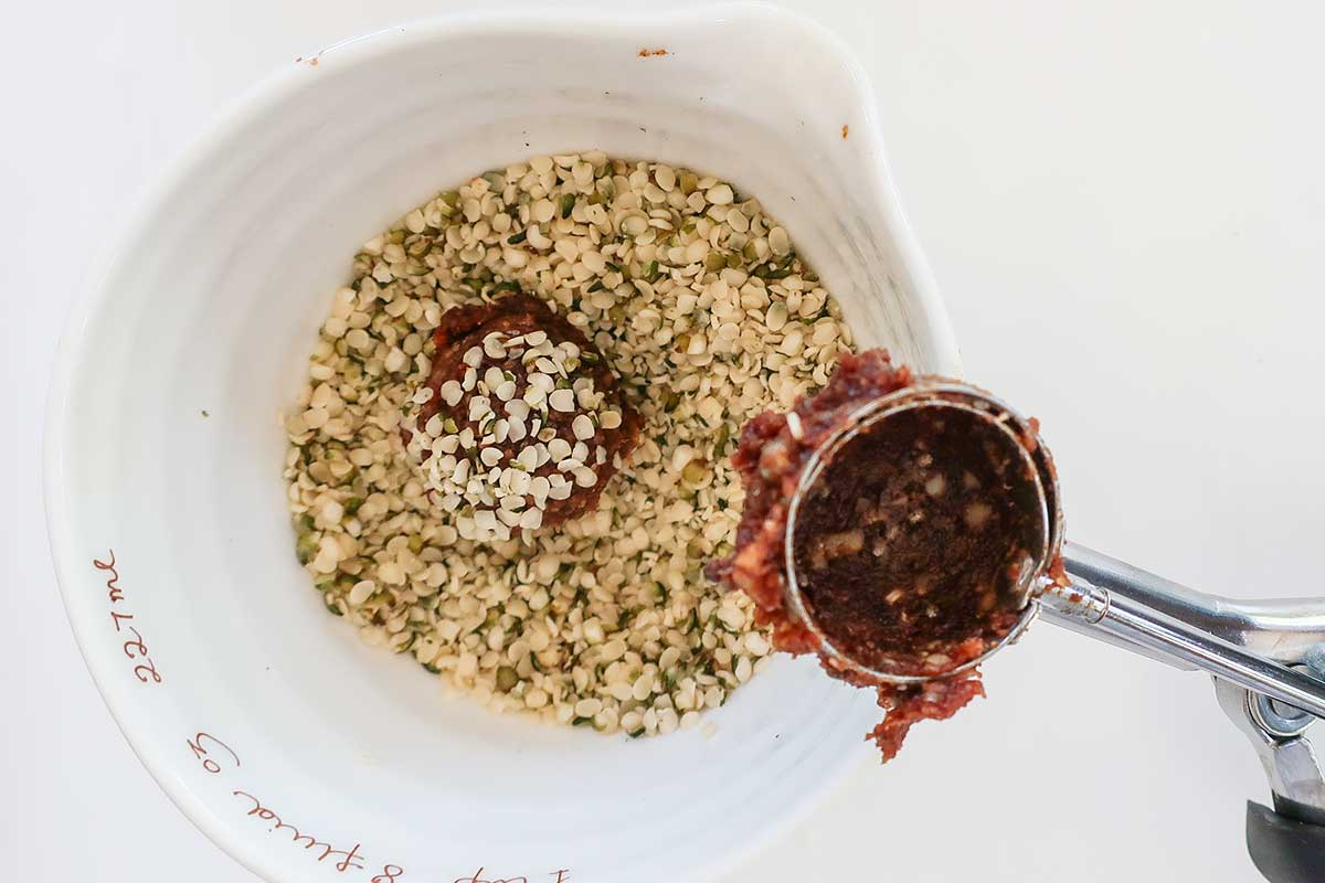 a small bowl filled with hemp seeds coating one ball of the protein mixture 