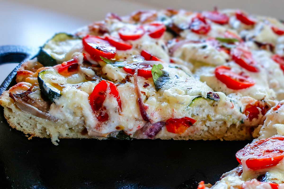 Close-up slice of baked gluten-free cast iron vegetable pizza showing melted cheese and roasted vegetables
