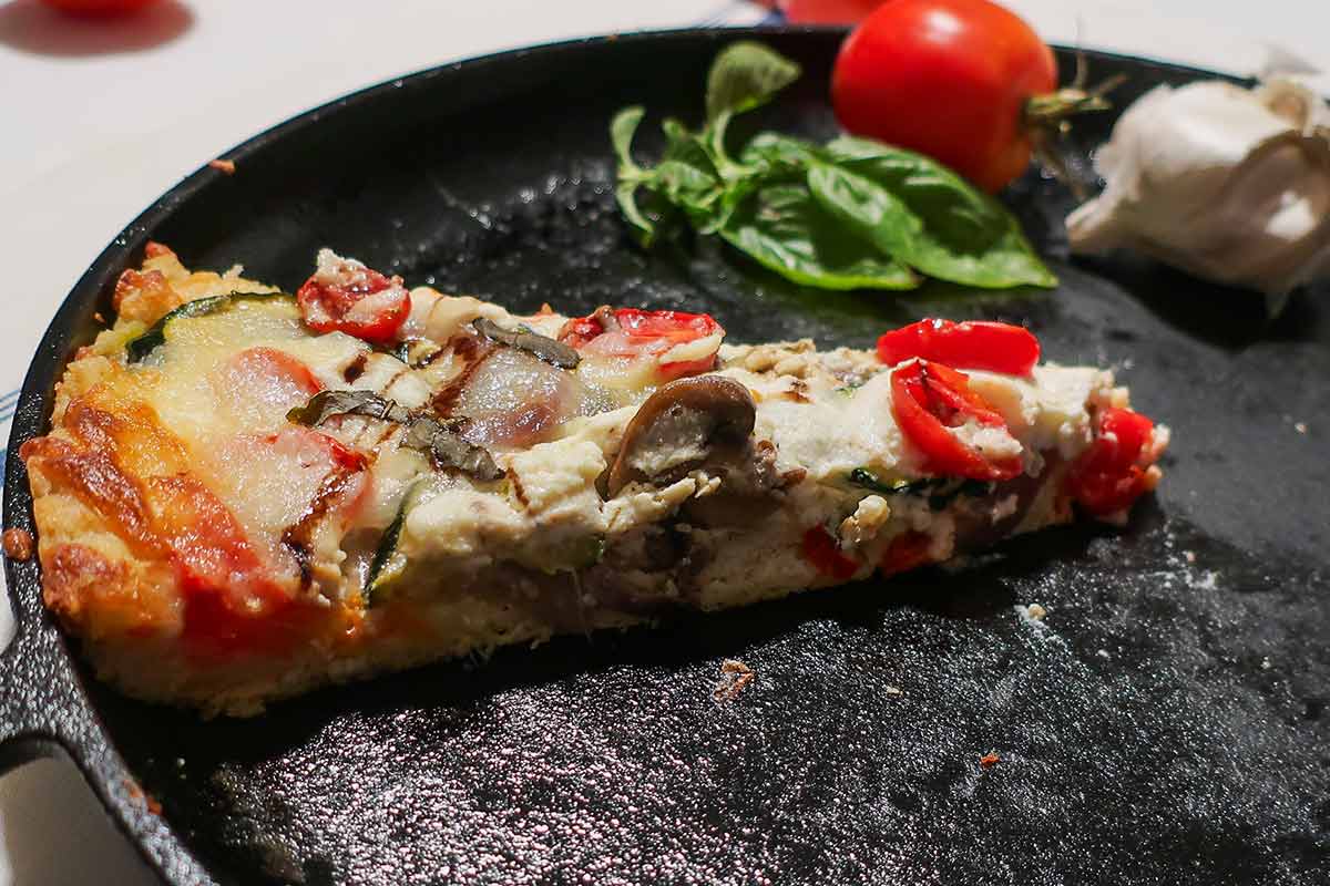 one baked slice of rustic pizza on a cast iron skillet showing the texture of the crumb and toppings