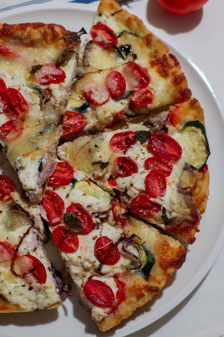 Sliced rustic gluten-free cast iron vegetable pizza with ricotta and roasted vegetables