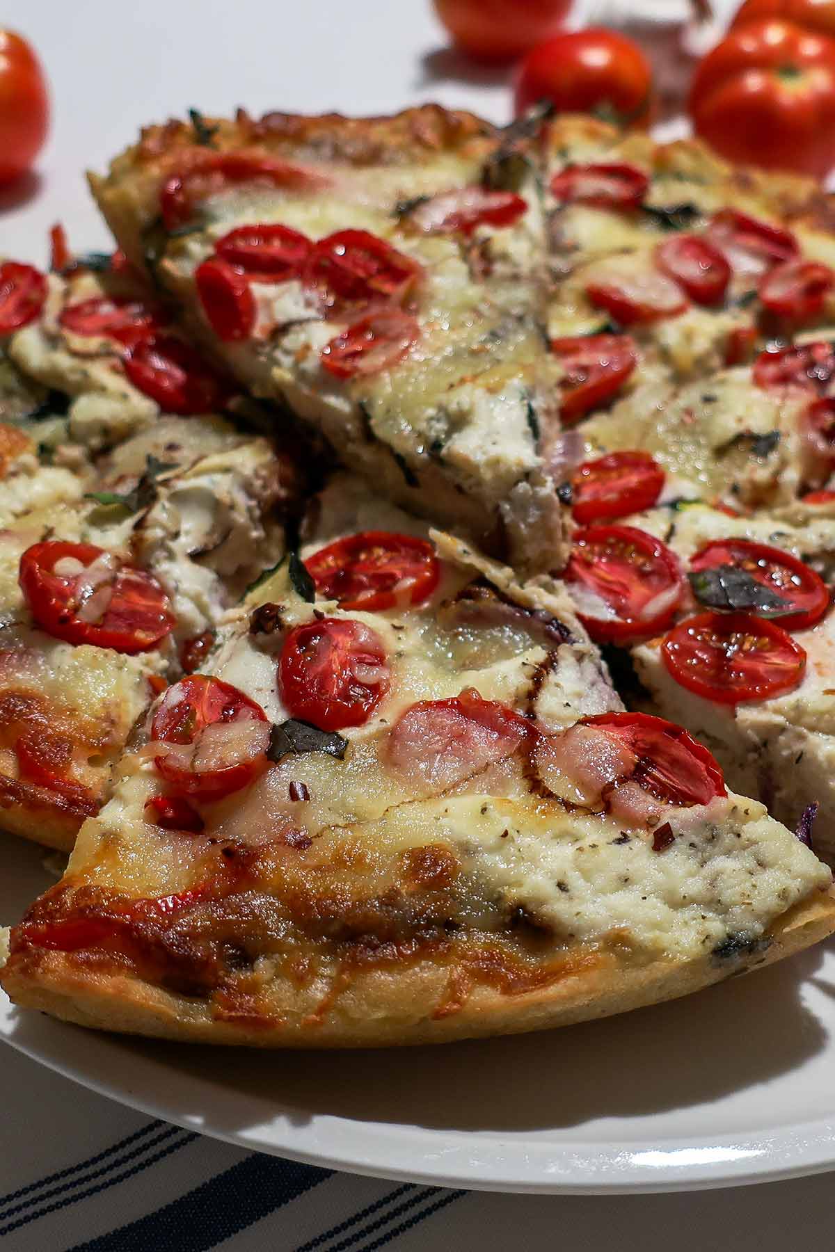 Close-up slice of baked gluten-free cast iron vegetable pizza showing melted cheese and roasted vegetables on a plate