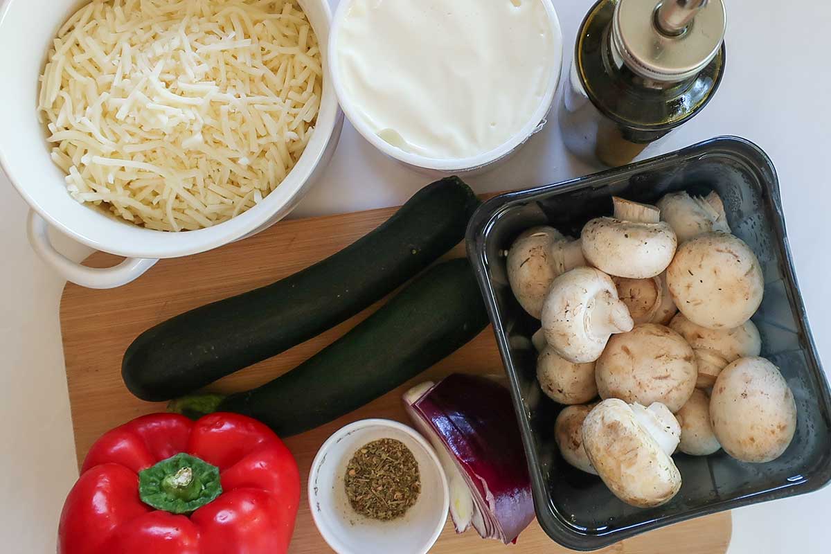 Ingredients for gluten-free cast iron roasted vegetable pizza including, ricotta, cheese, zucchini, mushrooms, bell peppers, shredded cheese and spices