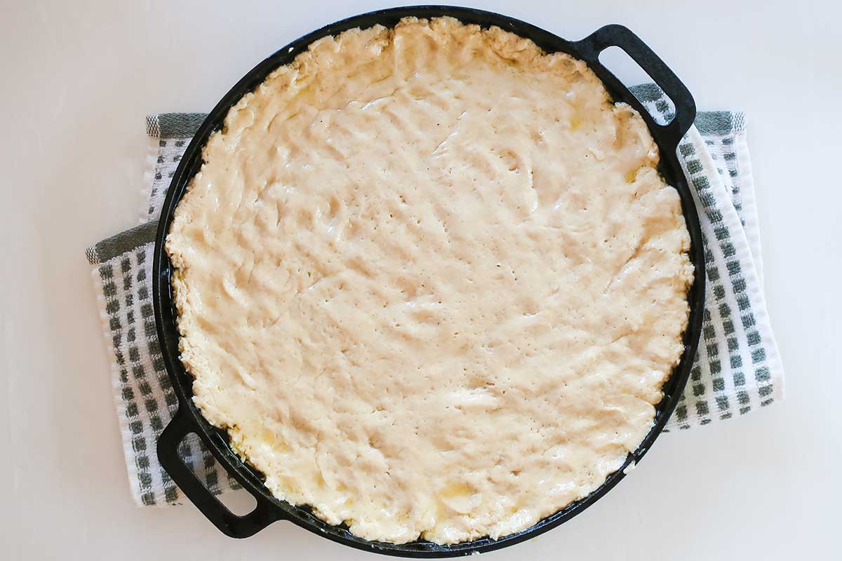 Gluten-free pizza dough spread evenly in an oiled cast iron skillet