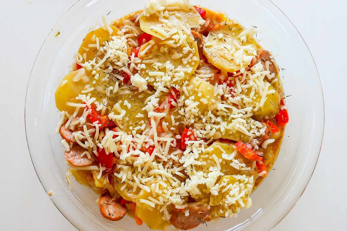 layered potatoes, sausage sautéed onion and peppers with sauce in a pie dish topped with shredded cheese before baking