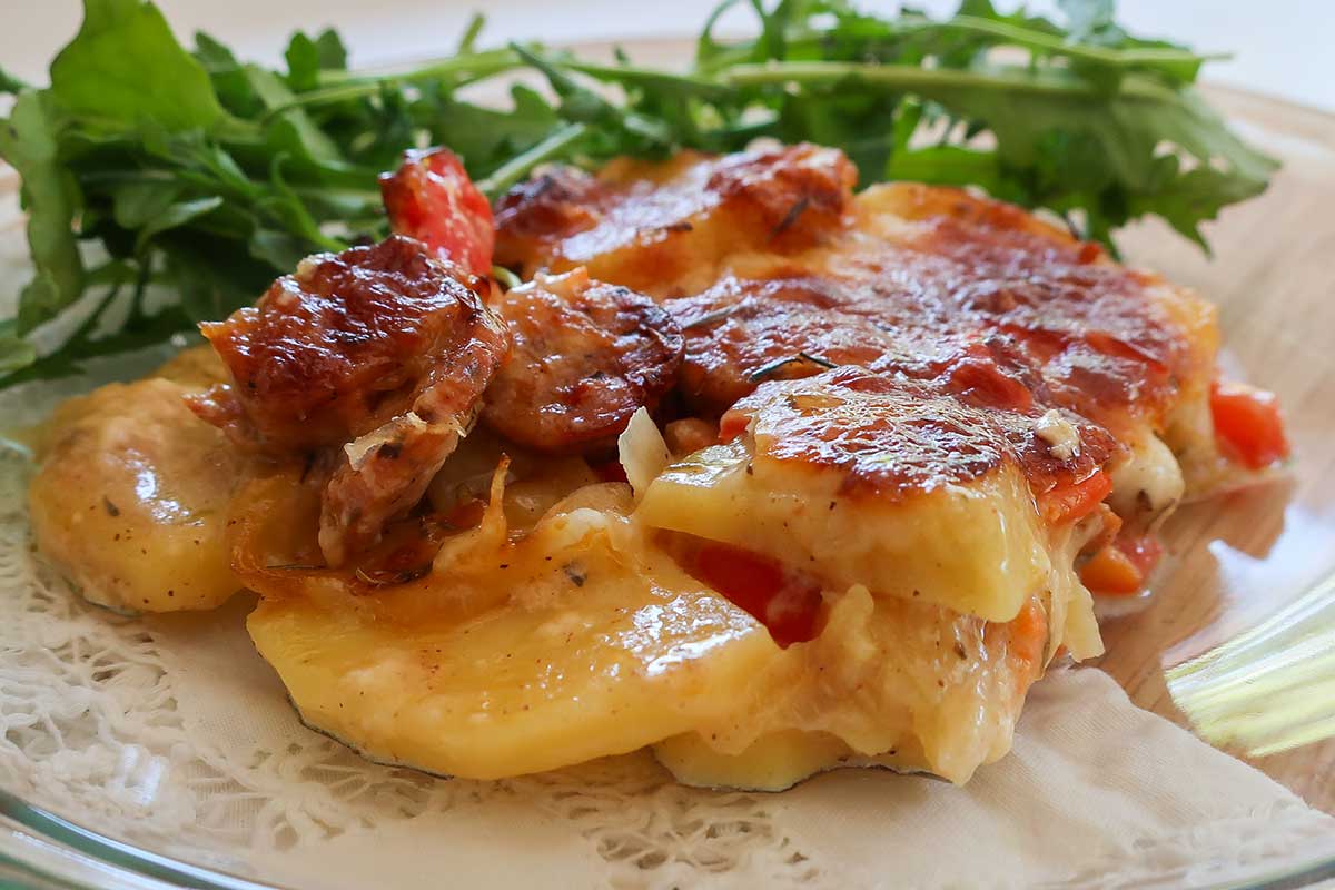 close up of a slice of cheesy sausage potato bake with greens on a plate
