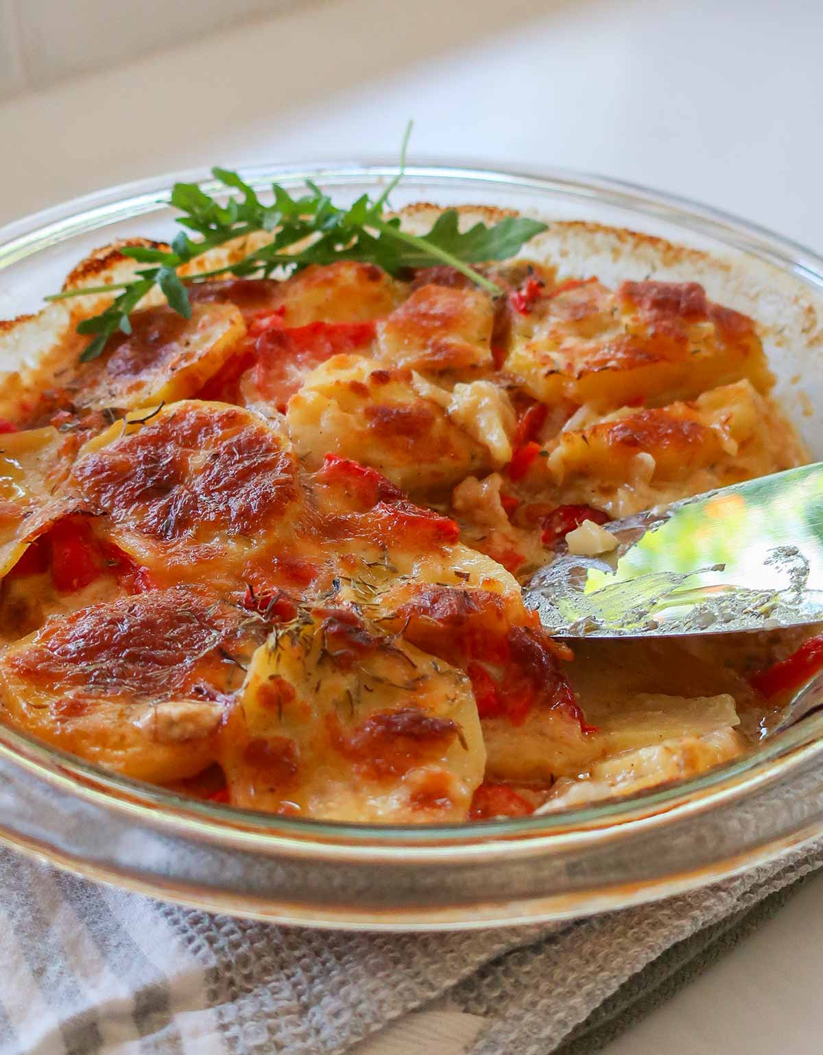 close up of freshly baked cheesy sausage potato bake in a pie dish with a serving spoon