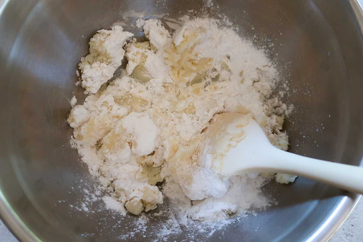 A close-up view of mixing leftover mashed potatoes, potato starch, and salt together in a bowl to form a simple gluten-free gnocchi dough.