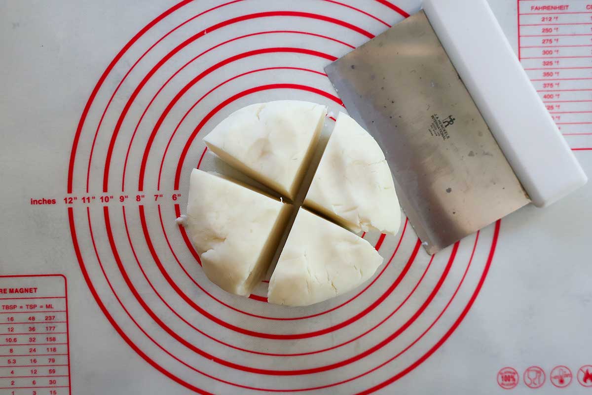 A smooth, round ball of grain-free potato gnocchi dough cut evenly into quarters on a lightly floured surface.