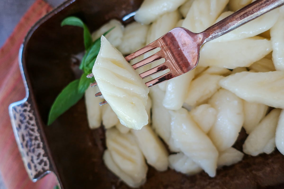 A close-up shot of a single cooked grain-free gnocchi on a fork, showing its light and pillowy texture over a dish of fresh gnocchi.