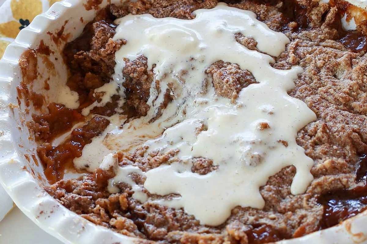 baked apricot cobbler style dump cake in a pie dish showing one slice missing and topped with melted vanilla ice cream