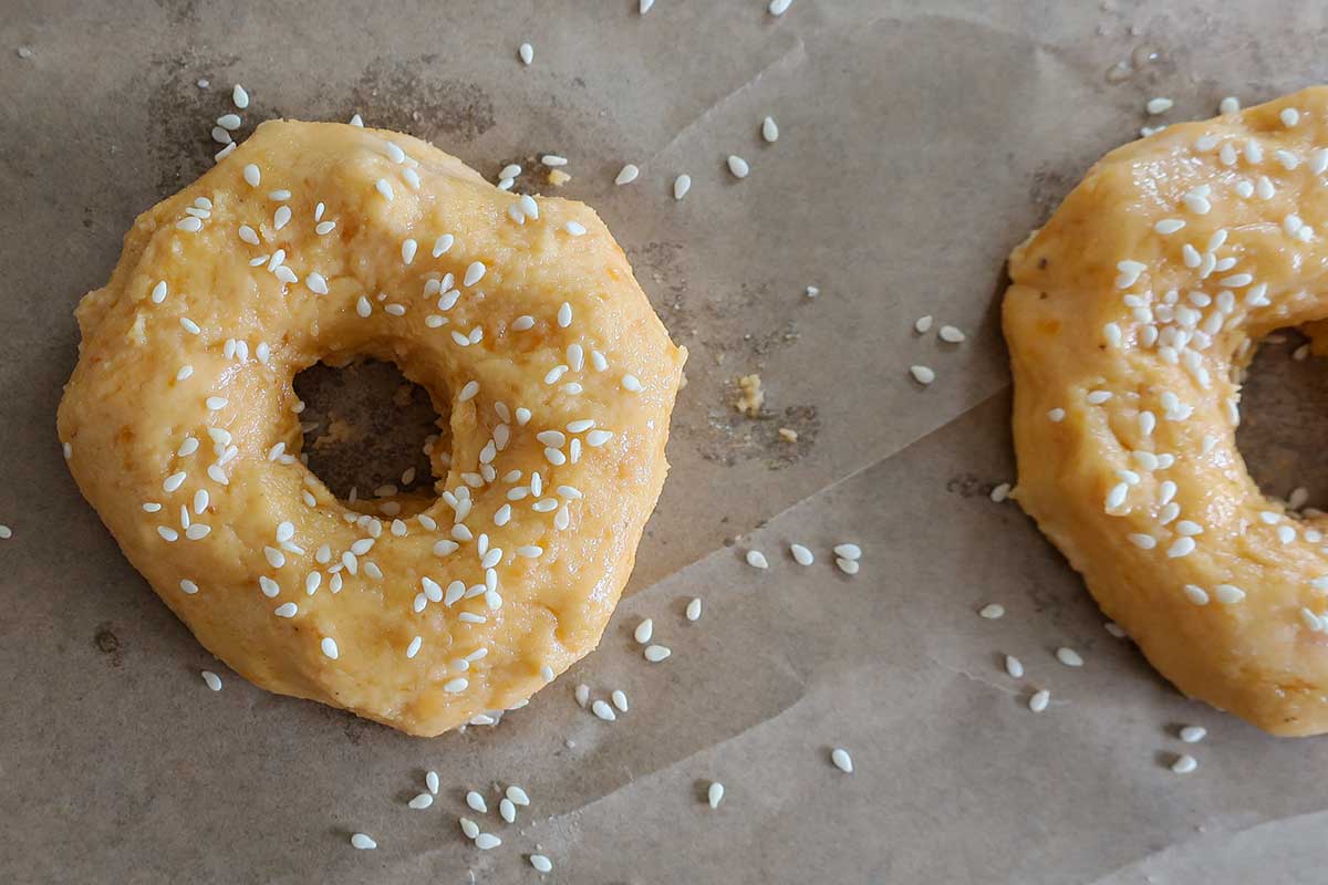 shaped bagels topped with sesame seeds on a baking sheet before baking