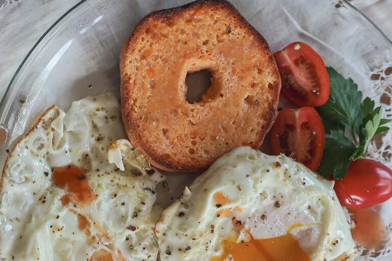 Grain-Free Low-Carb Bagel sliced in half showing dense crumb with 2 poached eggs on the side on a plate
