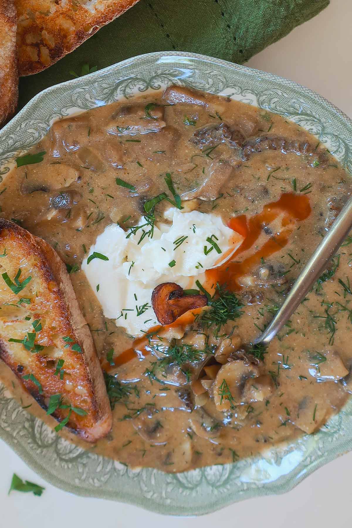 bowl of rich authentic Hungarian creamy mushroom soup topped with sour cream, fresh dill and slice of toasted GF Italian bread