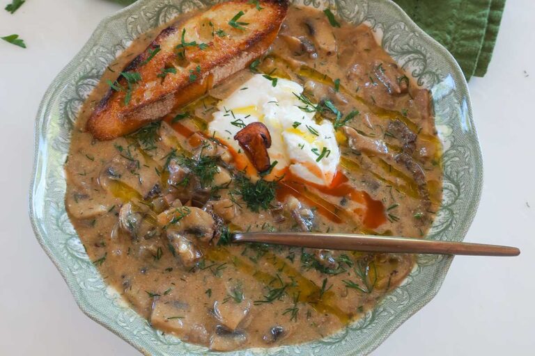 bowl of rich authentic Hungarian creamy mushroom soup topped with sour cream, fresh dill and slice of toasted GF Italian bread