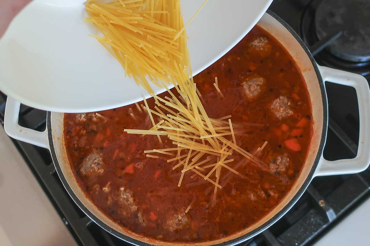 Adding the broken in pieces of spaghetti to the soup broth with meatballs