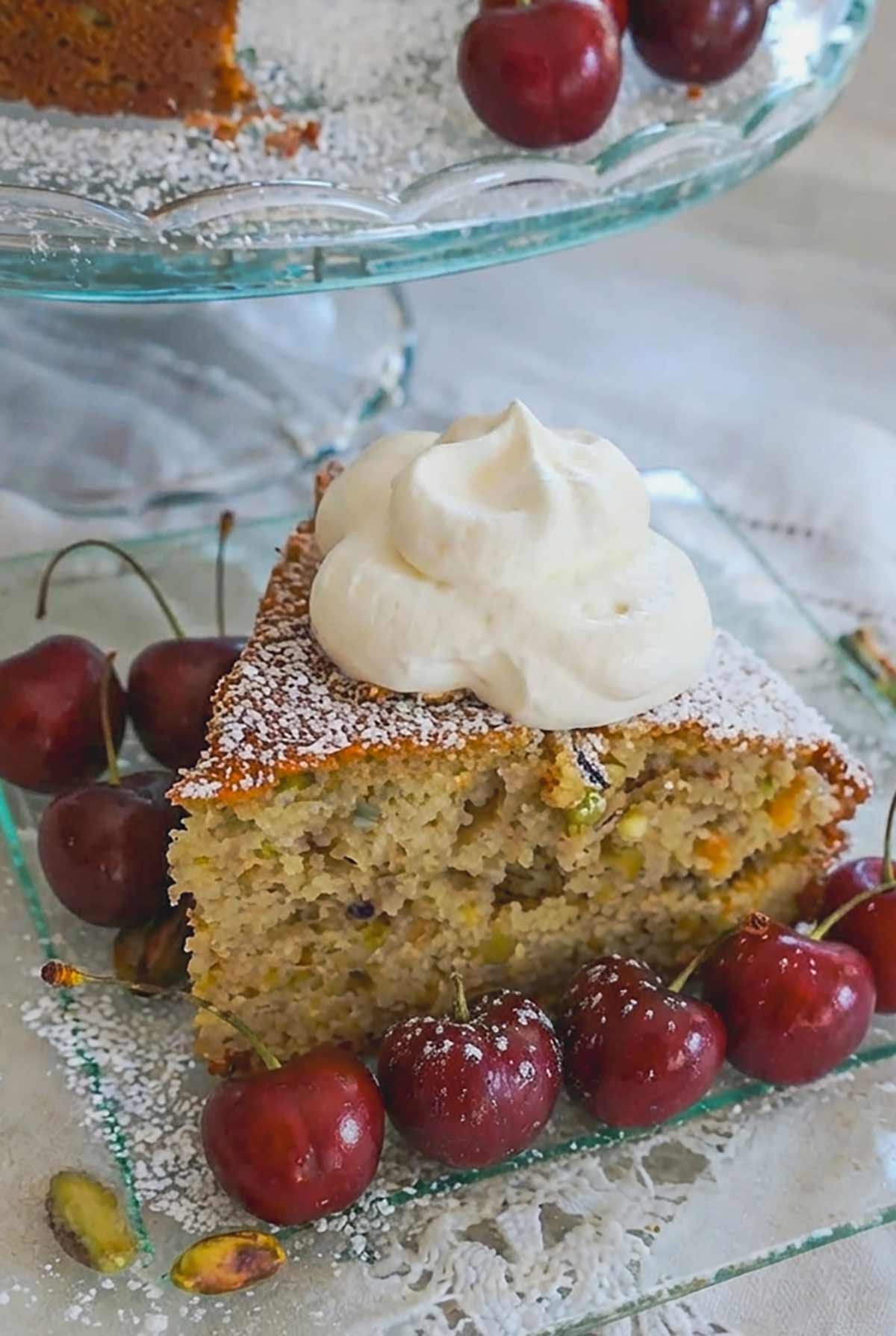 slice of pistachio lemon cake with a side of cherries and topped with whipped cream