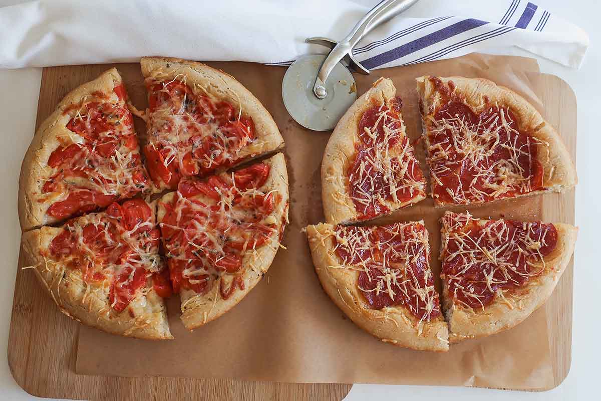 Two 9" freshly baked pizzas with crispy crust, one with pepperoni the other with tomatoes, both have same amount of cheese.