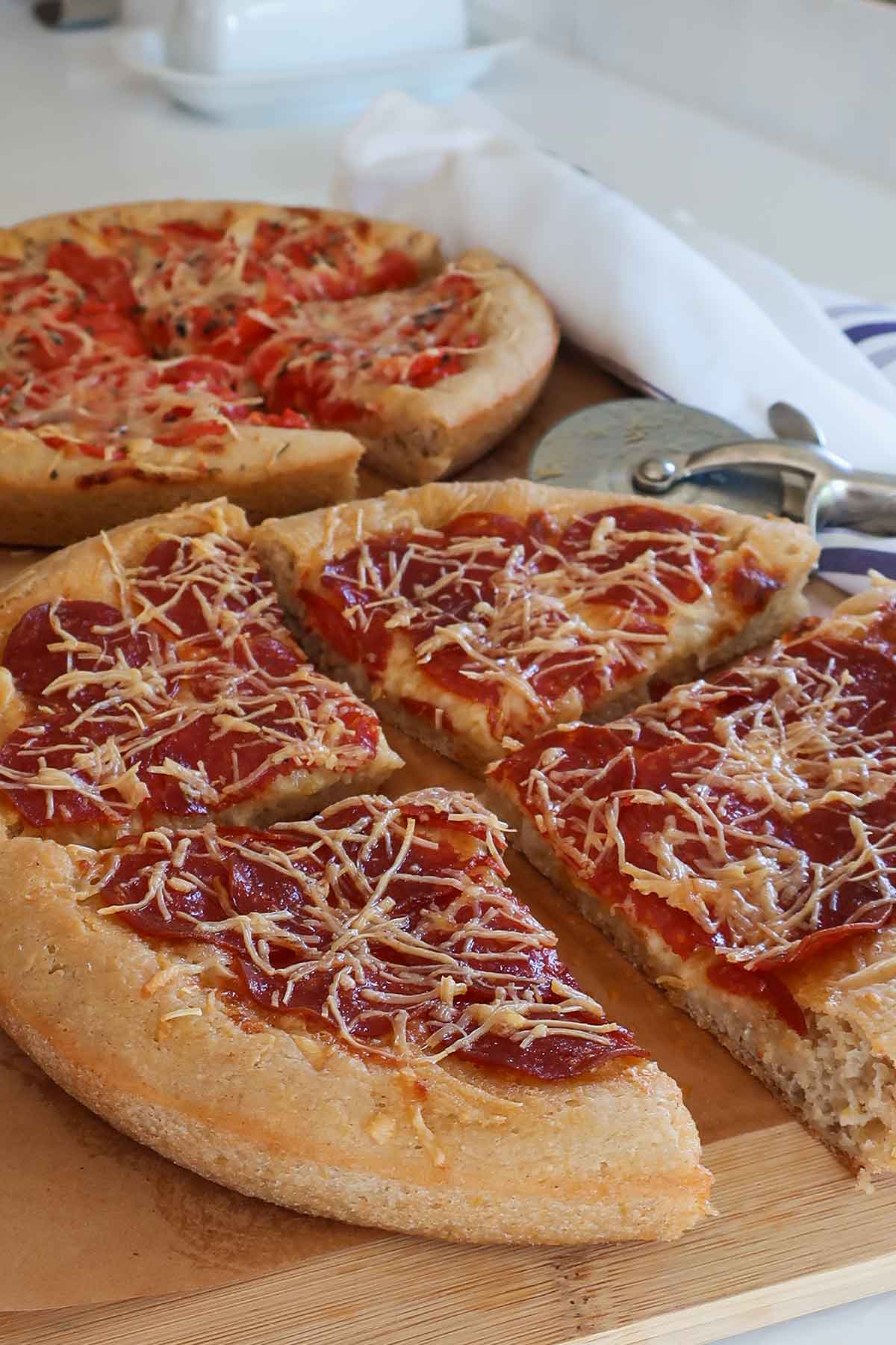 2 whole, freshly baked gluten-free Chicago deep dish pizza with a golden olive oil crust, topped with fresh tomatoes, melted mozzarella, and crispy pepperoni on a wooden board