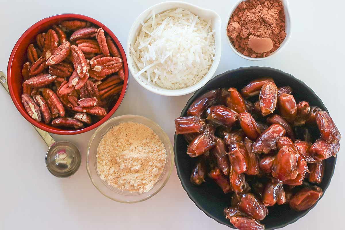 bowls of pecans, dates, coconut flour, cocoa powder and shredded coconut