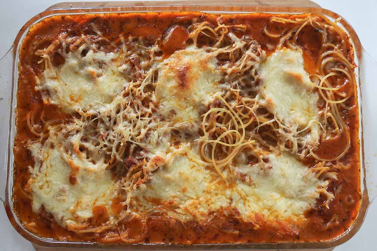 Freshly baked Gluten-Free Million Dollar Spaghetti Bake with sauce on the sides and melted dollops of cheese on top with some crispy spaghetti strands peaking through