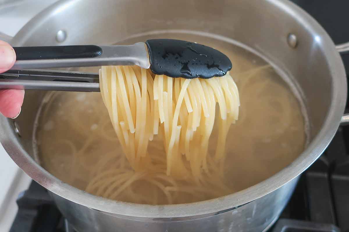 showing undercooked slightly firm pasta removed from the boiling water using thongs