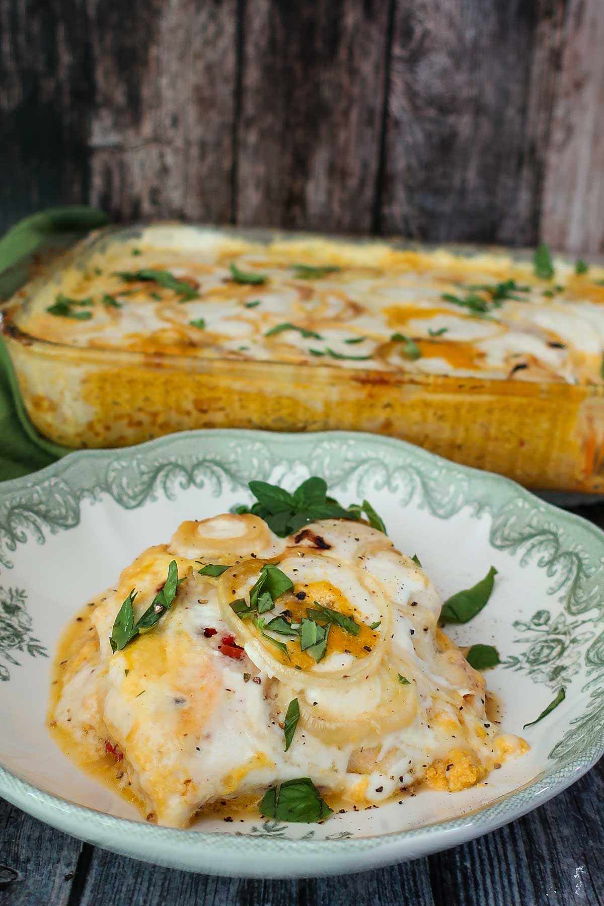 close up of a slice of Grain-Free Sweet Potato Lasagna with Creamy Pumpkin Ricotta on a plate with fresh basil leaves